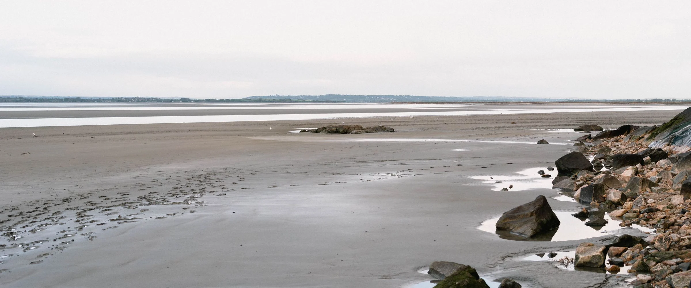 A quiet beach at low tide with rocks along the shore